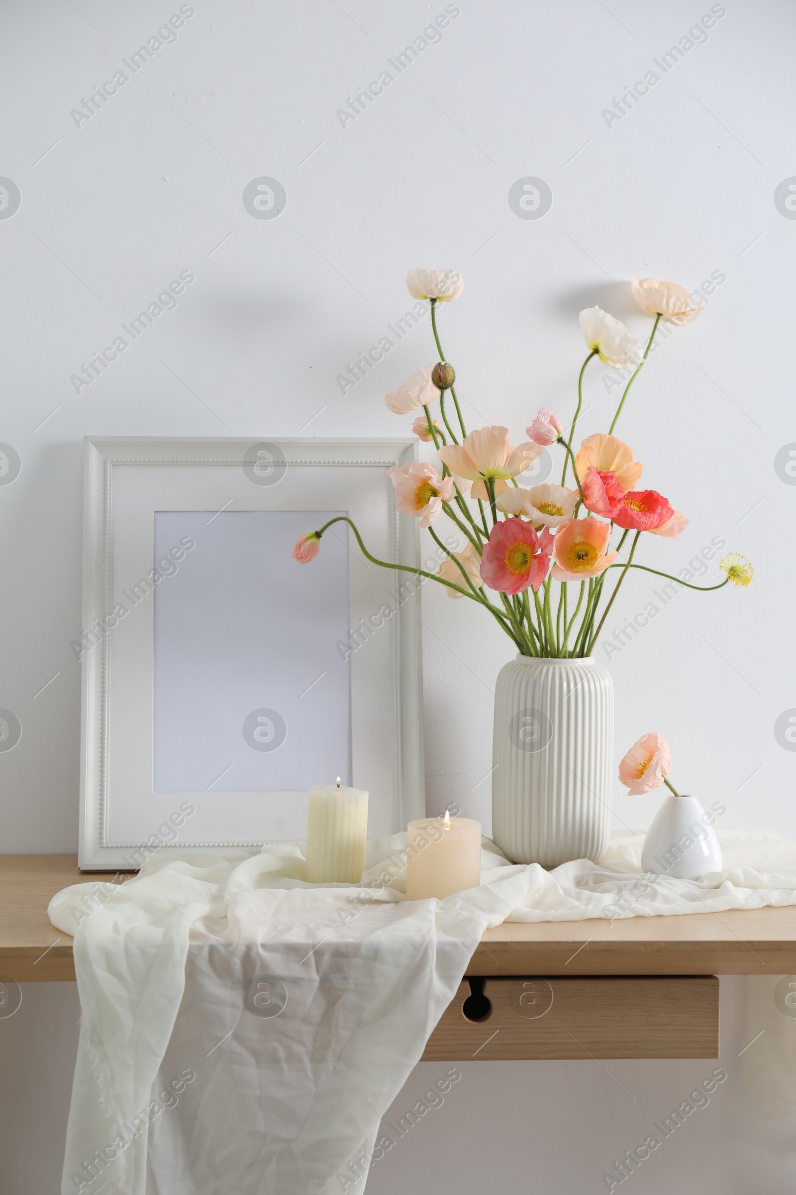 Bouquet of beautiful poppy flowers, frame and burning candles on table indoors Photo of Bouquet of beautiful poppy flowers, frame and burning candles on table indoors