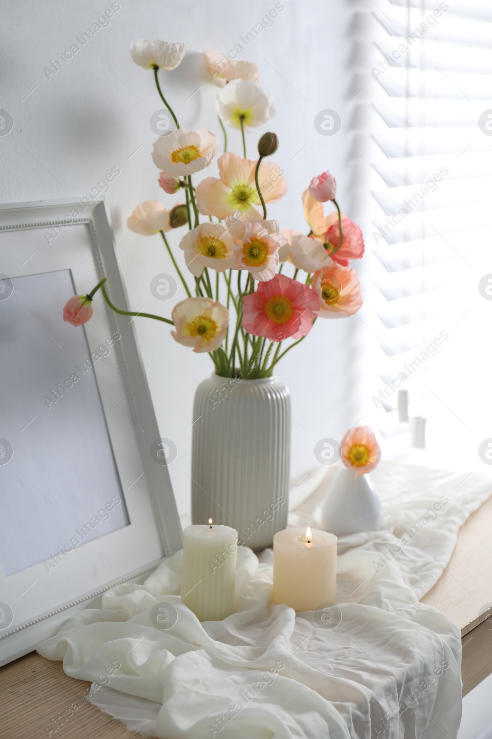 Bouquet of beautiful poppy flowers, frame and burning candles on table indoors Photo of Bouquet of beautiful poppy flowers, frame and burning candles on table indoors