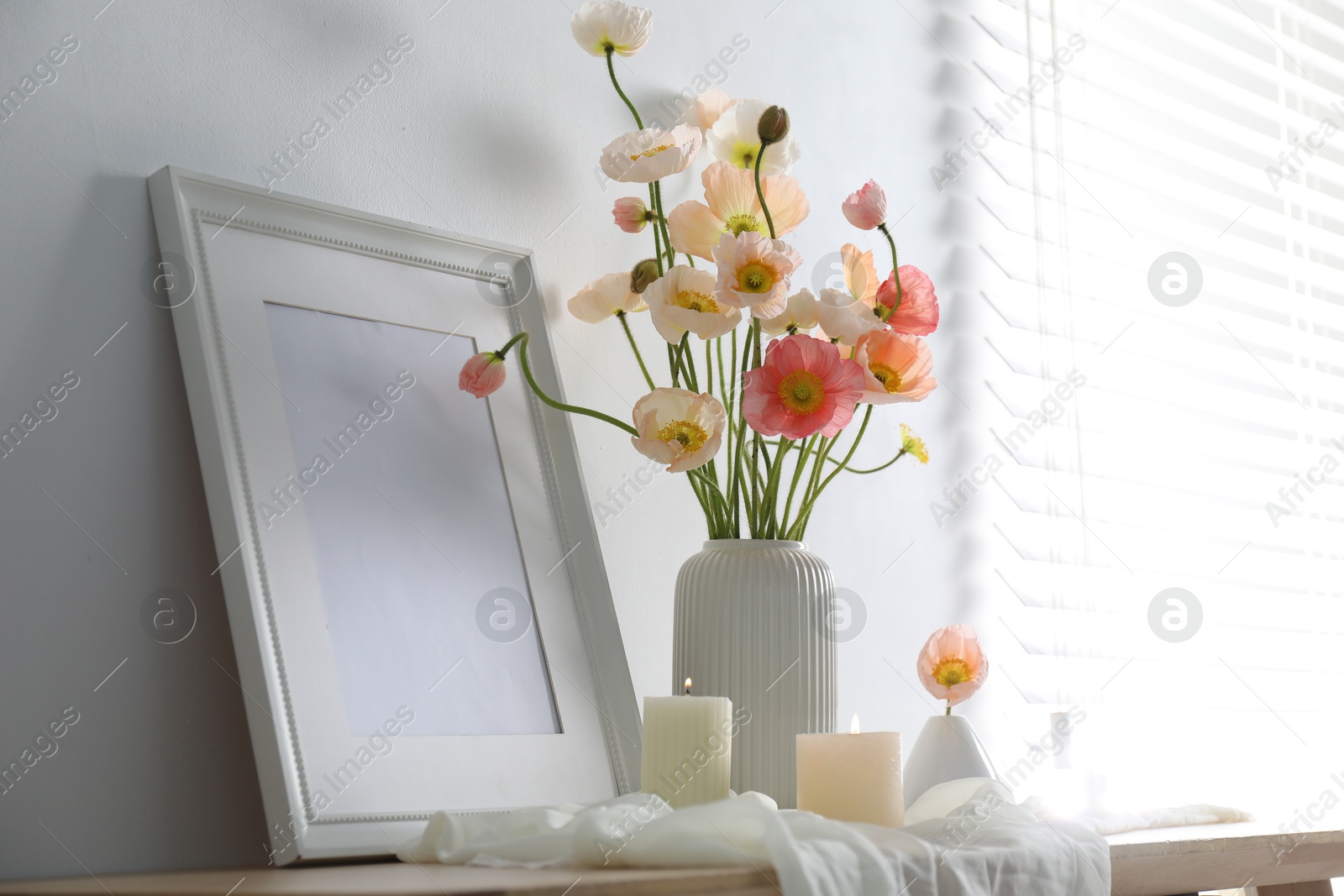 Bouquet of beautiful poppy flowers, frame and burning candles on table indoors Photo of Bouquet of beautiful poppy flowers, frame and burning candles on table indoors