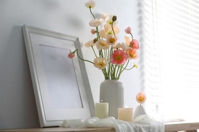Photo of Bouquet of beautiful poppy flowers, frame and burning candles on table indoors