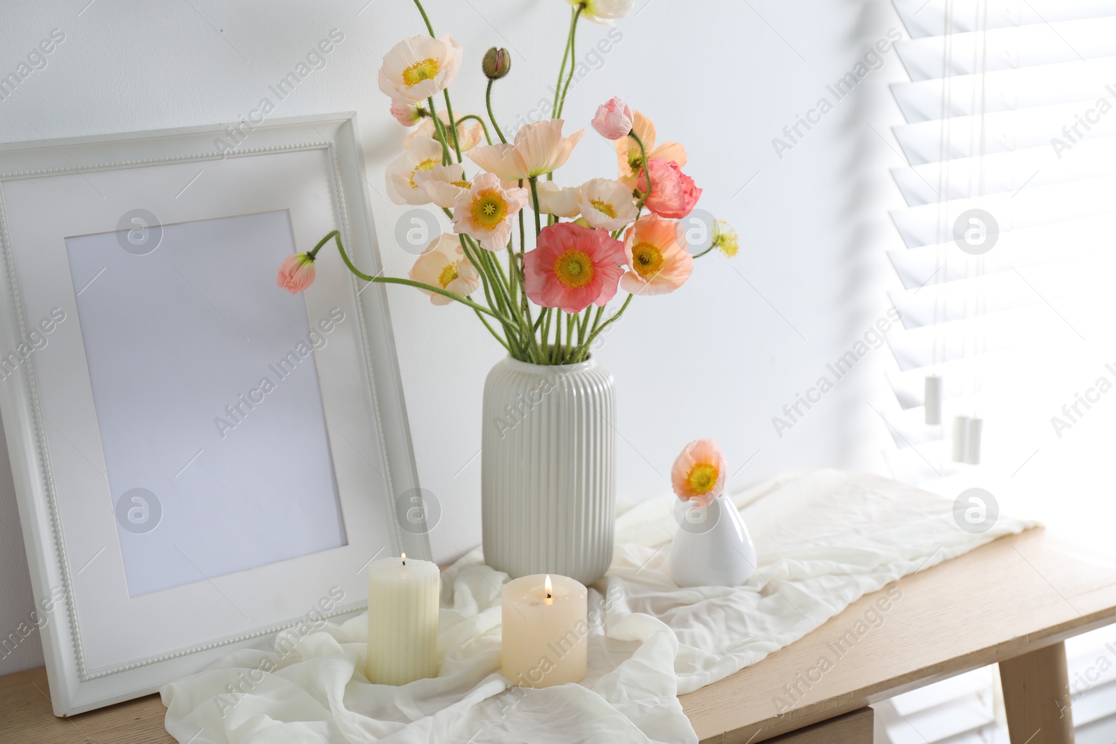 Bouquet of beautiful poppy flowers, frame and burning candles on table indoors Photo of Bouquet of beautiful poppy flowers, frame and burning candles on table indoors