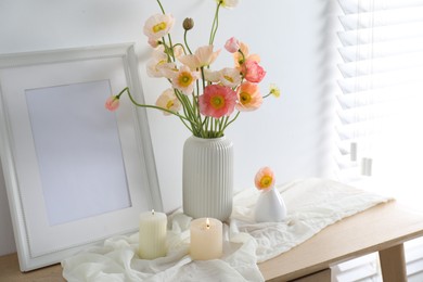 Photo of Bouquet of beautiful poppy flowers, frame and burning candles on table indoors