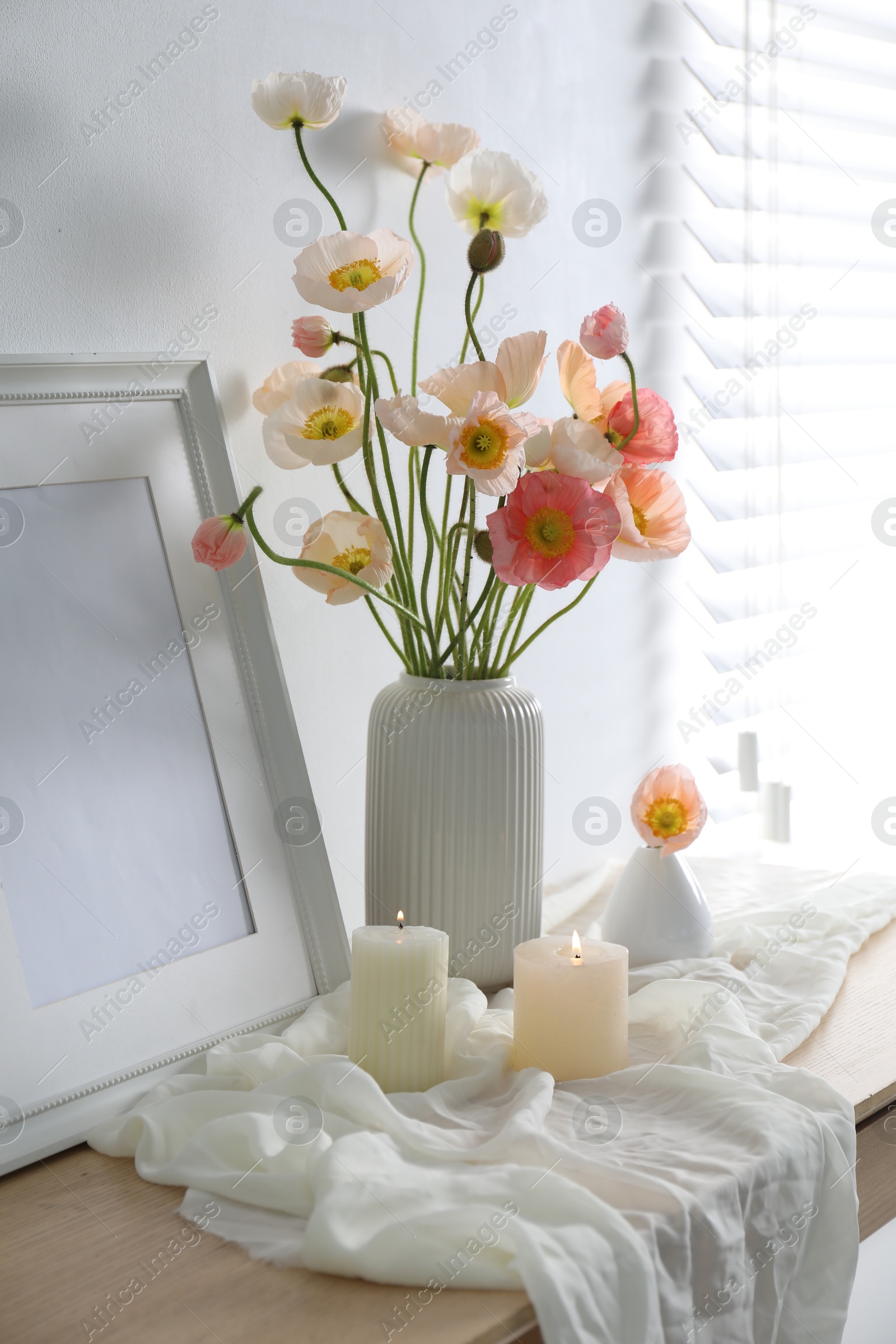 Bouquet of beautiful poppy flowers, frame and burning candles on table indoors Photo of Bouquet of beautiful poppy flowers, frame and burning candles on table indoors