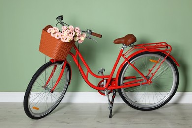 Photo of Bicycle with basket of beautiful flowers near light green wall indoors