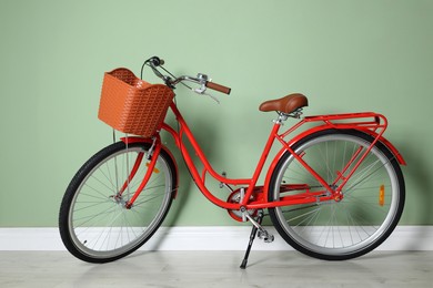 Photo of Red bicycle with basket near light green wall indoors