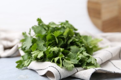 Photo of Fresh aromatic cilantro and towel on light grey table, closeup