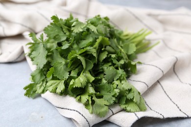 Photo of Fresh aromatic cilantro and towel on light grey table, closeup