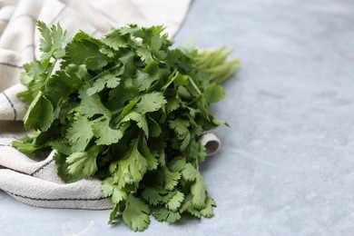 Photo of Fresh aromatic cilantro and towel on light grey table, closeup. Space for text