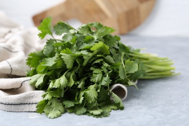 Photo of Fresh aromatic cilantro and towel on light grey table, closeup