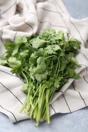 Photo of Fresh aromatic cilantro and towel on light grey table, closeup