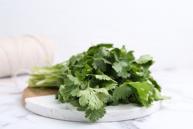Photo of Fresh aromatic cilantro, cutting board and thread on white marble table, closeup