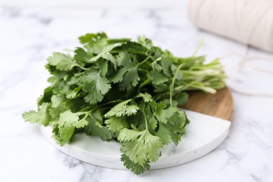 Photo of Fresh aromatic cilantro, cutting board and thread on white marble table, closeup