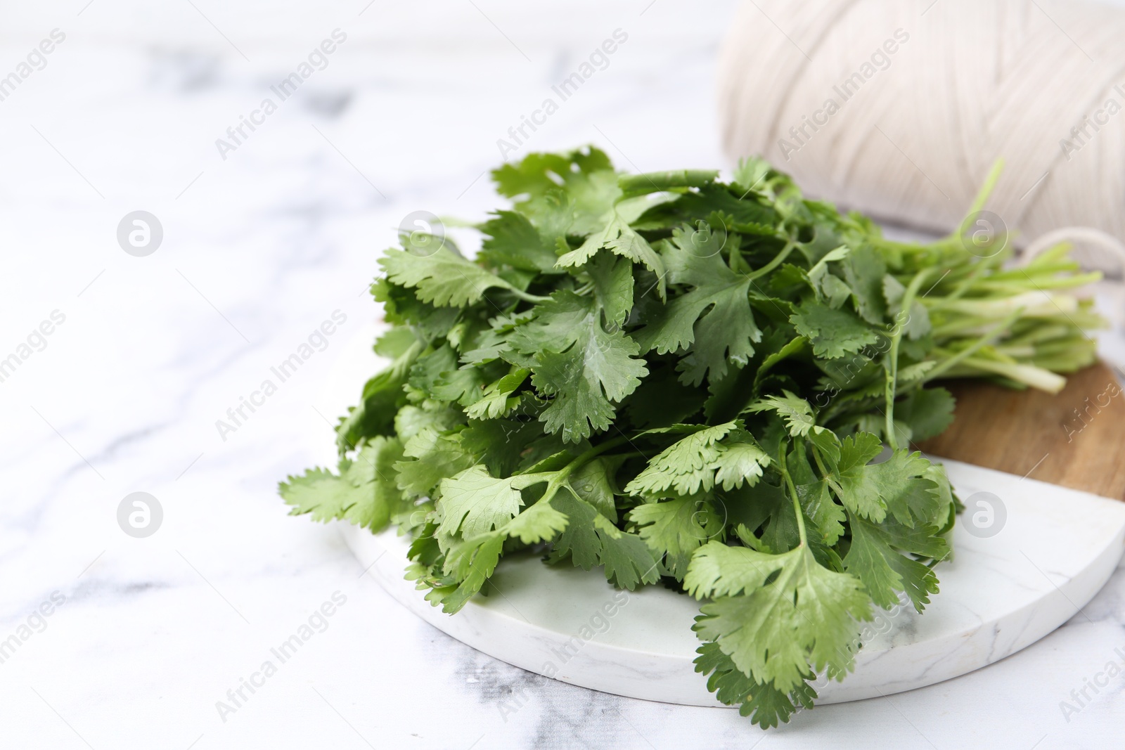 Fresh aromatic cilantro, cutting board and thread on white marble table, closeup. Space for text Photo of Fresh aromatic cilantro, cutting board and thread on white marble table, closeup. Space for text