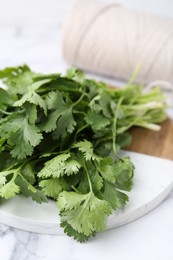 Photo of Fresh aromatic cilantro, cutting board and thread on white marble table, closeup