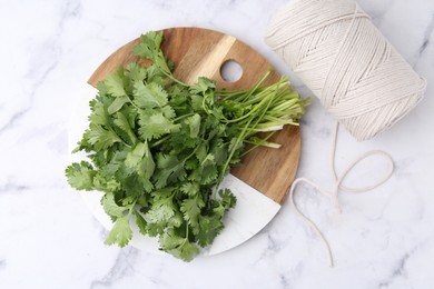 Photo of Fresh aromatic cilantro, cutting board and thread on white marble table, top view