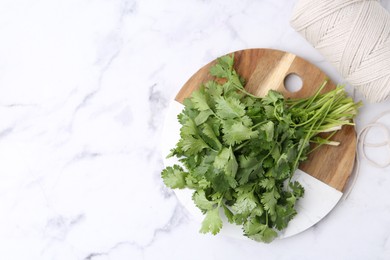 Photo of Fresh aromatic cilantro, cutting board and thread on white marble table, top view. Space for text