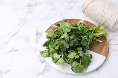 Photo of Fresh aromatic cilantro, cutting board and thread on white marble table. Space for text