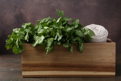 Photo of Fresh aromatic cilantro and thread in crate on wooden table