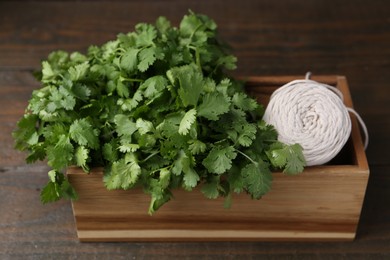 Photo of Fresh aromatic cilantro and thread in crate on wooden table, closeup