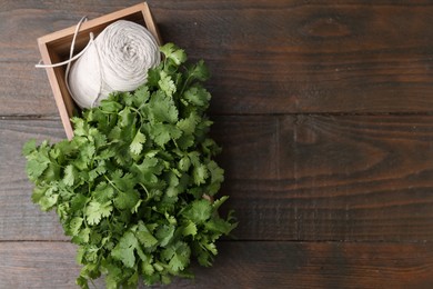 Photo of Fresh aromatic cilantro and thread in crate on wooden table, top view. Space for text