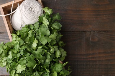 Photo of Fresh aromatic cilantro and thread in crate on wooden table, top view. Space for text