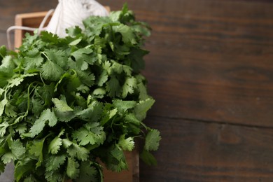 Photo of Fresh aromatic cilantro and thread in crate on wooden table, closeup. Space for text