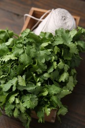 Photo of Fresh aromatic cilantro and thread in crate on wooden table, closeup