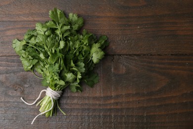 Photo of Bunch of fresh aromatic cilantro on wooden table, top view. Space for text