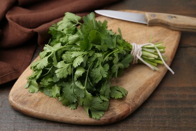 Photo of Cutting board with fresh cilantro and knife on wooden table, closeup
