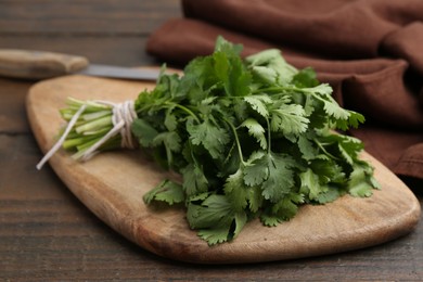 Photo of Cutting board with fresh cilantro and knife on wooden table, closeup