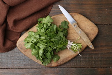 Photo of Cutting board with fresh cilantro and knife on wooden table, top view