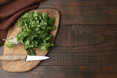 Photo of Cutting board with fresh cilantro and knife on wooden table, top view. Space for text