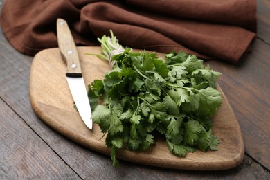 Photo of Cutting board with fresh cilantro and knife on wooden table, closeup