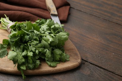 Photo of Cutting board with fresh cilantro and knife on wooden table, closeup. Space for text