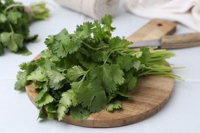 Photo of Cutting board with fresh cilantro and knife on white table, closeup