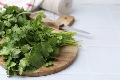 Photo of Cutting board with fresh cilantro and knife on white tiled table, closeup. Space for text