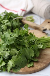 Photo of Cutting board with fresh cilantro and knife on white table, closeup