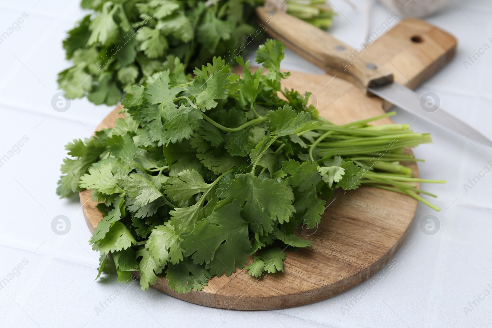Cutting board with fresh cilantro and knife on white table, closeup Photo of Cutting board with fresh cilantro and knife on white table, closeup