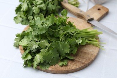Photo of Cutting board with fresh cilantro and knife on white table, closeup