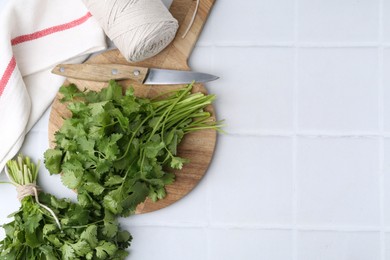 Photo of Cutting board with fresh cilantro and knife on white tiled table, flat lay. Space for text