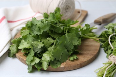 Photo of Cutting board with fresh cilantro and knife on white table, closeup
