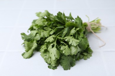 Photo of Bunch of fresh aromatic cilantro on white tiled table, closeup