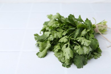 Photo of Bunch of fresh aromatic cilantro on white tiled table, closeup. Space for text