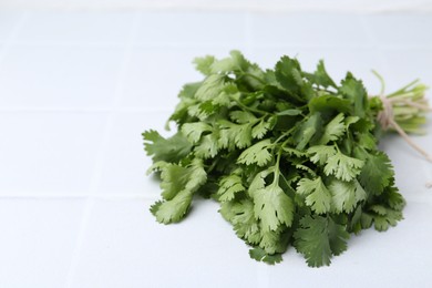 Photo of Bunch of fresh aromatic cilantro on white tiled table, closeup. Space for text