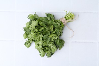 Photo of Bunch of fresh aromatic cilantro on white tiled table, top view