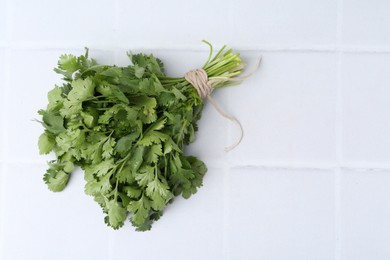 Photo of Bunch of fresh aromatic cilantro on white tiled table, top view. Space for text
