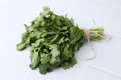 Photo of Bunch of fresh aromatic cilantro on white tiled table, closeup