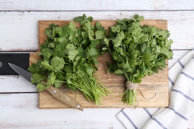 Photo of Cutting board with fresh cilantro and knife on white wooden table, top view