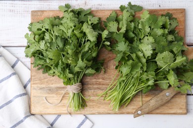 Photo of Cutting board with fresh cilantro and knife on white wooden table, top view