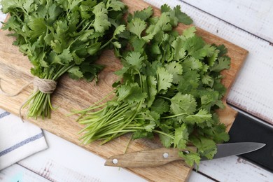 Photo of Cutting board with fresh cilantro and knife on white wooden table, top view